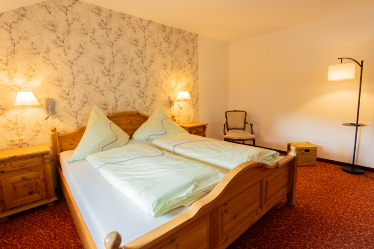 Ein Doppelbett mit zwei Nachtschränkchen und Wandlampen dazu roter Teppich und eine Stehlampe